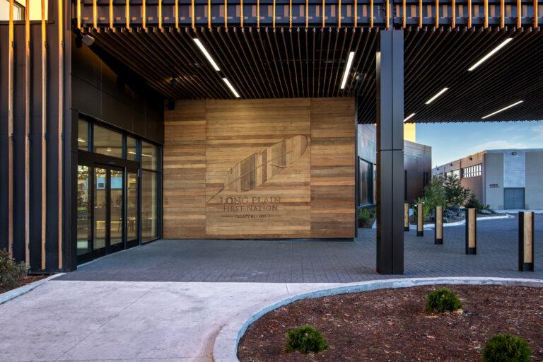 Hotel entrance with large wooden accent wall that includes a feather and 'Long Plain First Nation' etched into the wood.