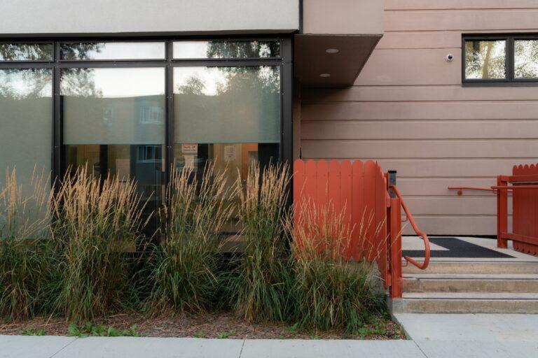 Exterior entry of building, with tall prairie grass in garden bed in front.