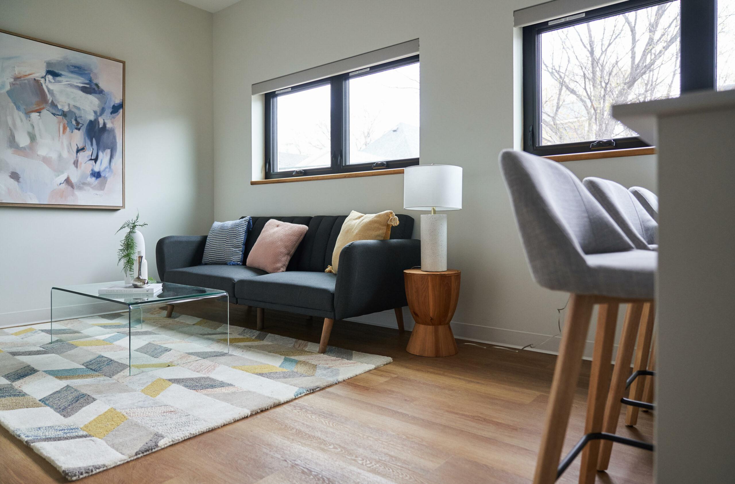 Living room with couch, coffee table, and rug, with perspective of the kitchen counter and bar stools.